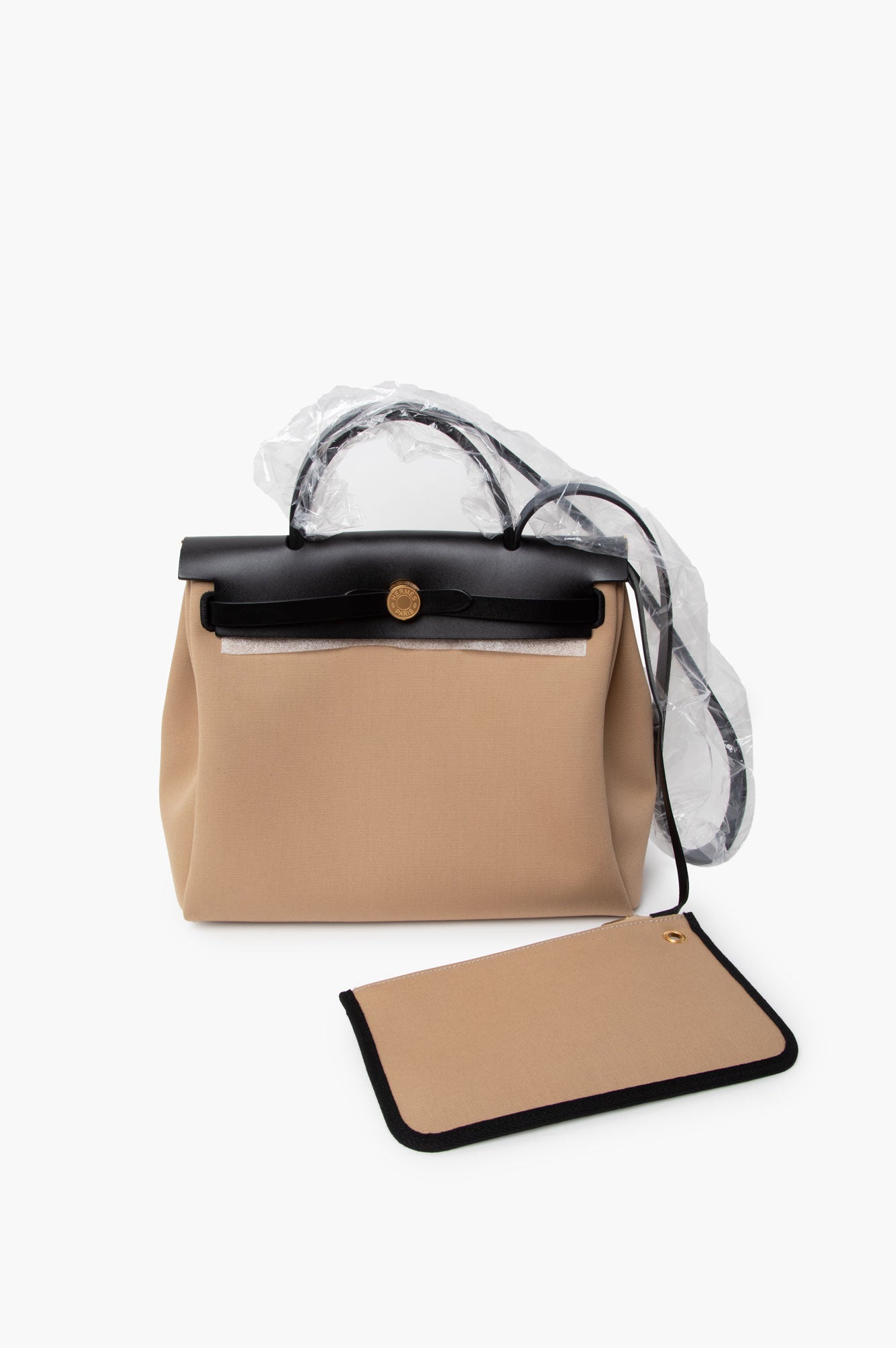 Hermes Beige Herbag 31 Shoulder Bag with protective plastic cover and Hermes clutch on a white surface.