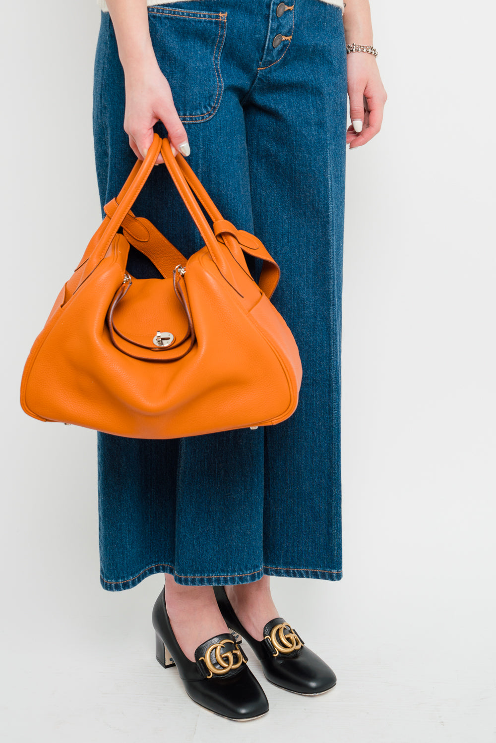 A woman holding a Hermes Orange Lindy 34 bag made from Clemence leather.
