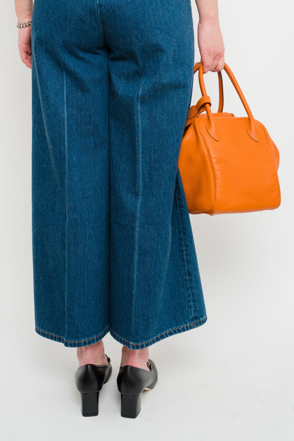 A back view of a woman holding a Hermes Orange Lindy 34 bag made from Clemence leather.