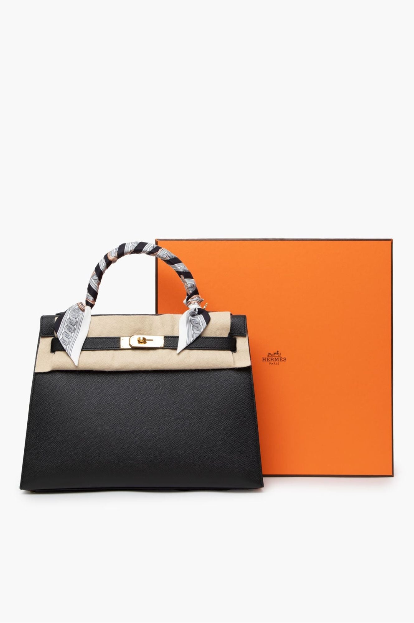 Stylish Hermes Kelly 32 Handbag Noir in Ardennes leather paired with gold hardware, accented with a silk scarf on the handle, set before the brand's signature orange box.