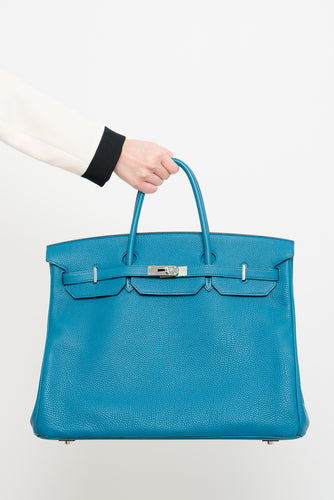 A person holding a Hermes Teal Birkin 40 Togo Leather bag by the handle, showcasing its fine grain texture and silver-tone hardware against a neutral background.